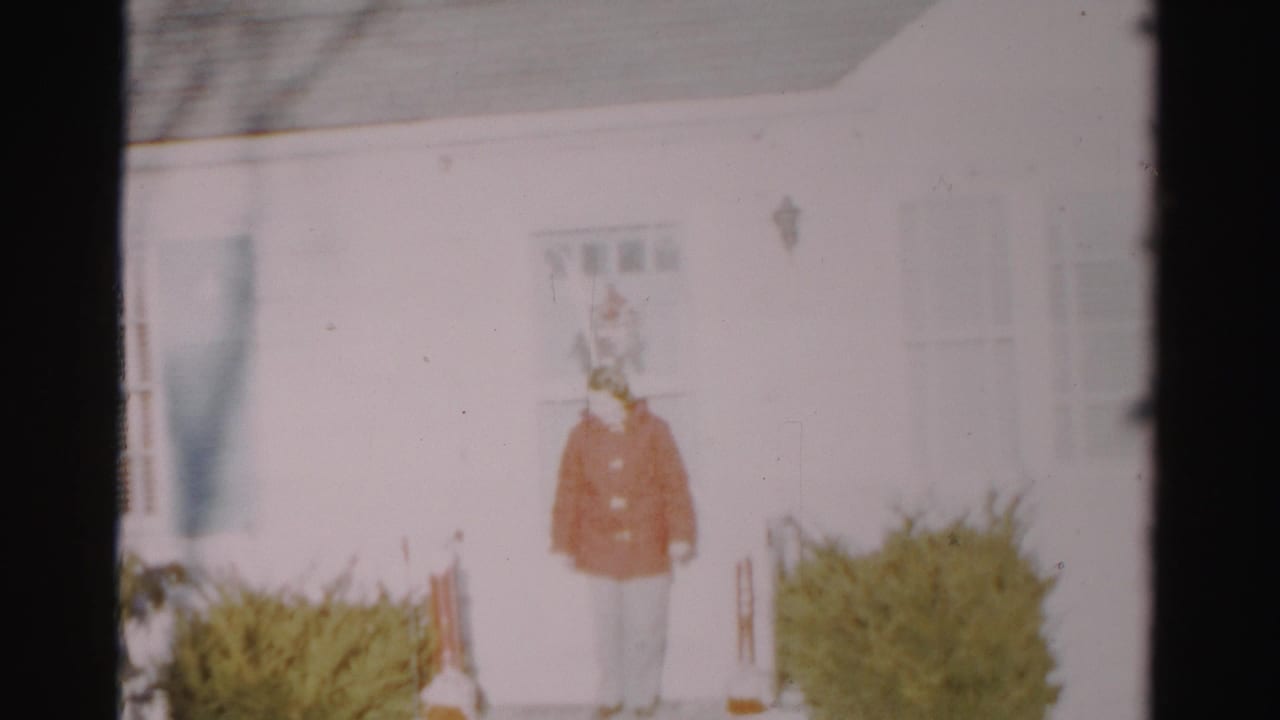 Woman in a red coat standing in front of a white house and shrubs.