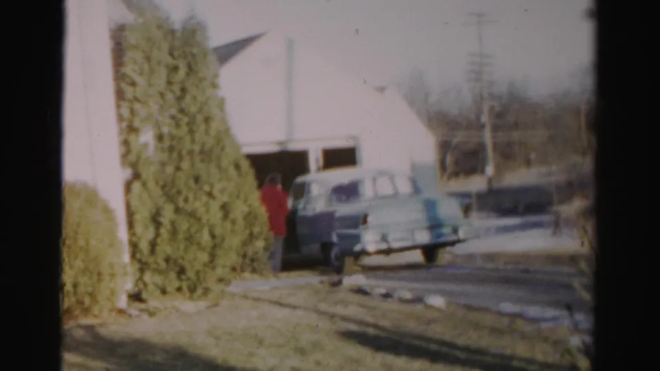 The woman is partly obscured by the car while standing by the door in the suburban Albany driveway.