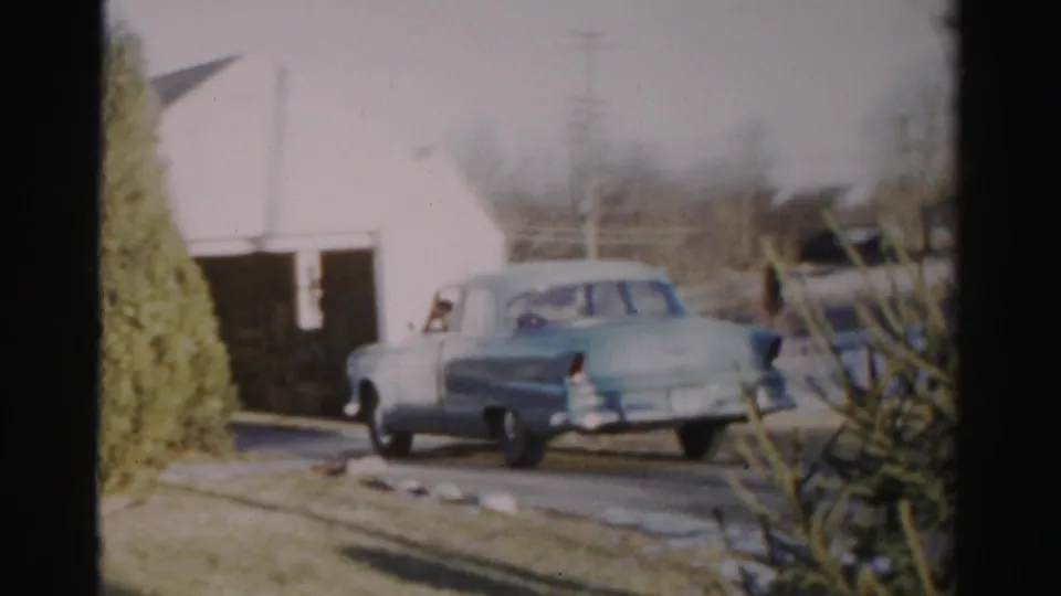 1956 Albany frame with the rear of a light blue sedan angled near the driveway and residential garage.