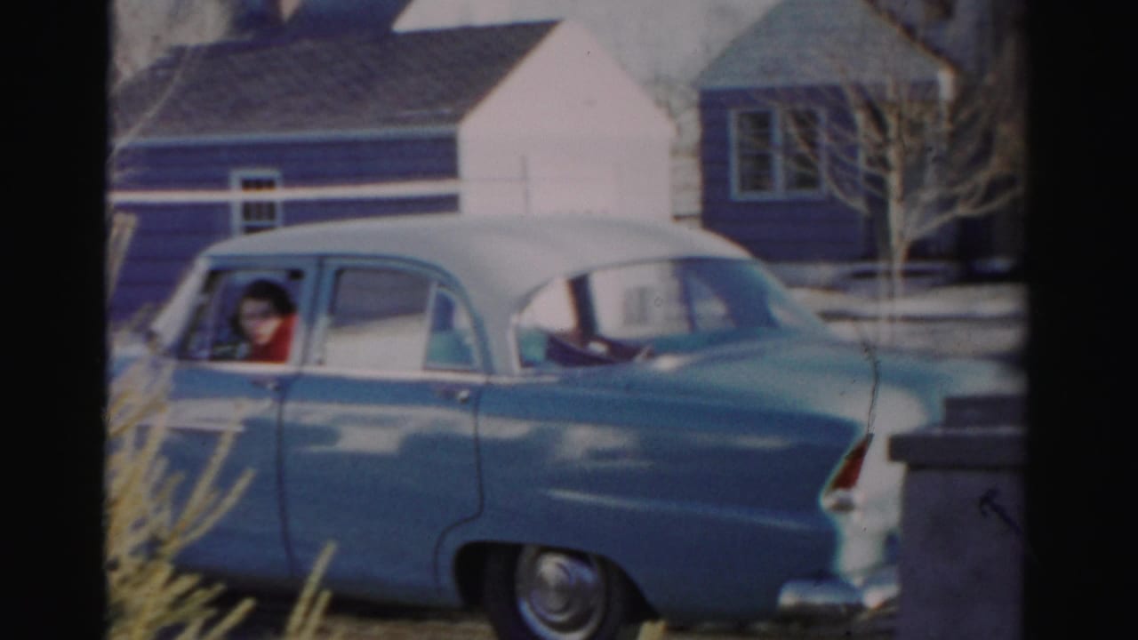 Blue sedan with white roof beside houses, with a woman visible through the driver window.