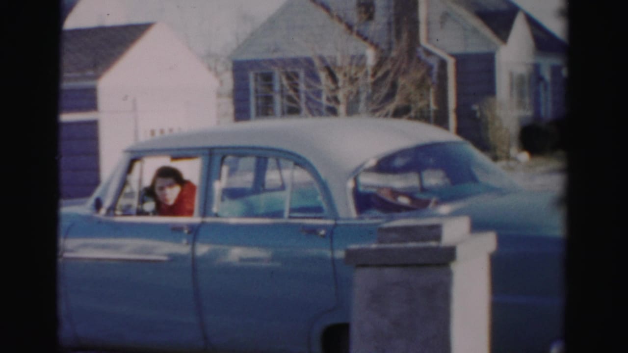 Blue-and-white sedan partly behind a porch post, with the driver visible through the window.