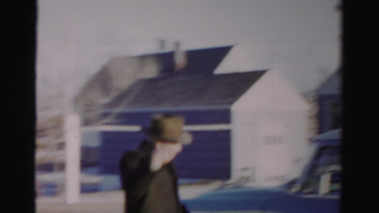 In Albany home-movie footage from the 1950s, a man in a fedora and dark coat waves beside a snowy residential street.