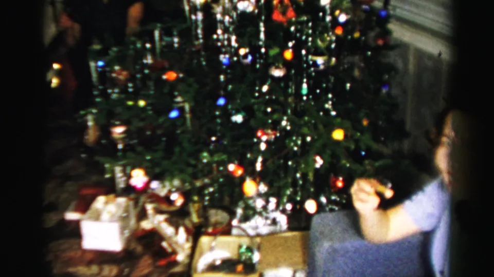 The decorated tree stands over wrapped gifts and boxes as a child appears at the edge of the 1956 Albany home-movie frame.
