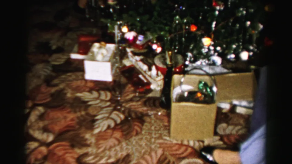 Albany 1956 home-movie frame showing a decorated tree, boxes and gift items on a patterned carpet in a private interior.