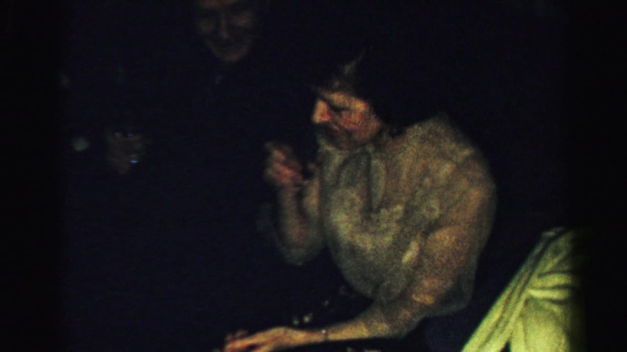 Woman seated in a dark room holding a small glass near her face.