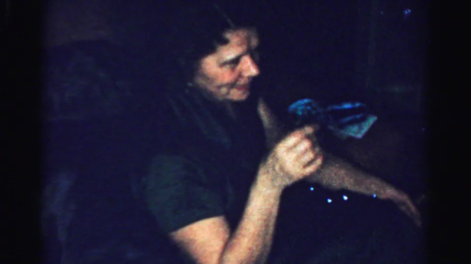 Profile view of an adult woman holding a glass in a shadowed 1950s Albany private-party home movie.