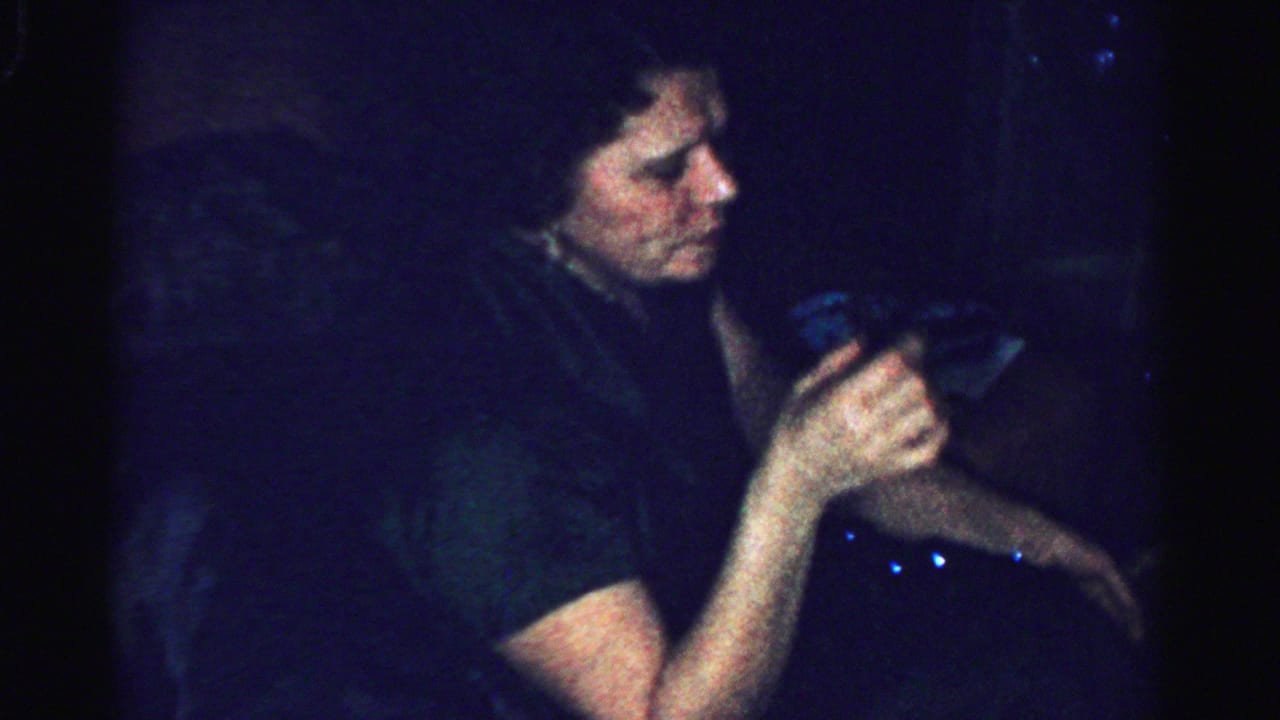 In a dim Albany home interior, a woman in a dark navy dress holds a glass near her face during the holiday gathering.