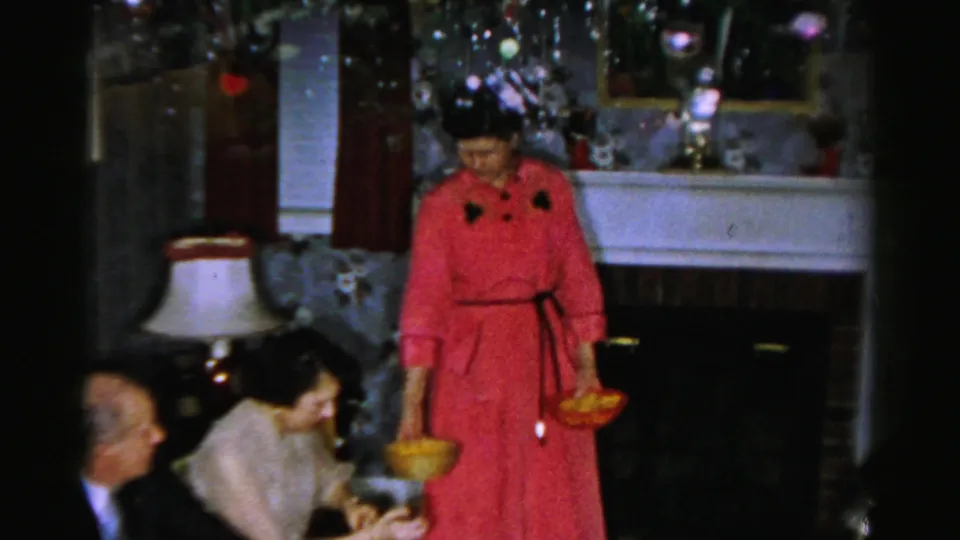 A woman in a red dress carries bowls through a living room while guests sit near a fireplace in the Albany home.