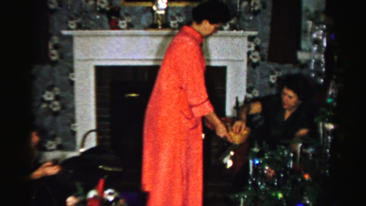 In a 1950s Albany home interior, a woman in a red dress serves a seated guest near a white mantel and holiday decorations.