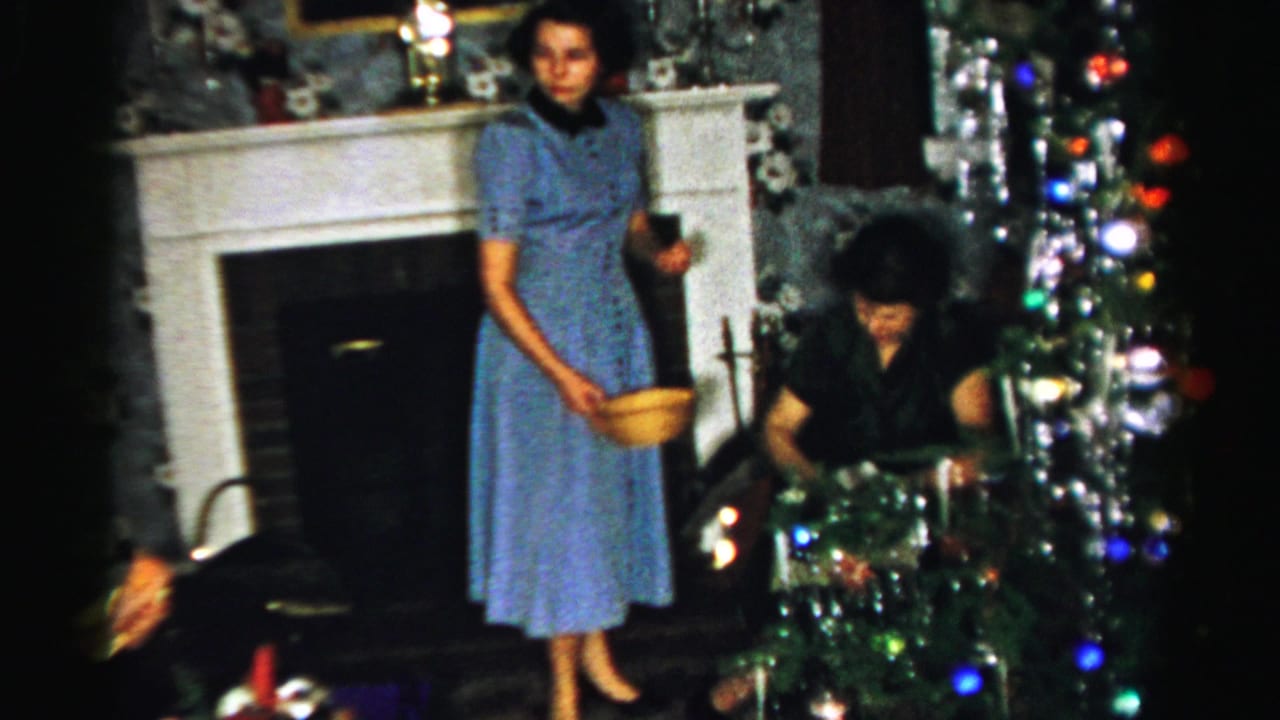 Woman in a blue dress stands with a yellow bowl beside a decorated Christmas tree.