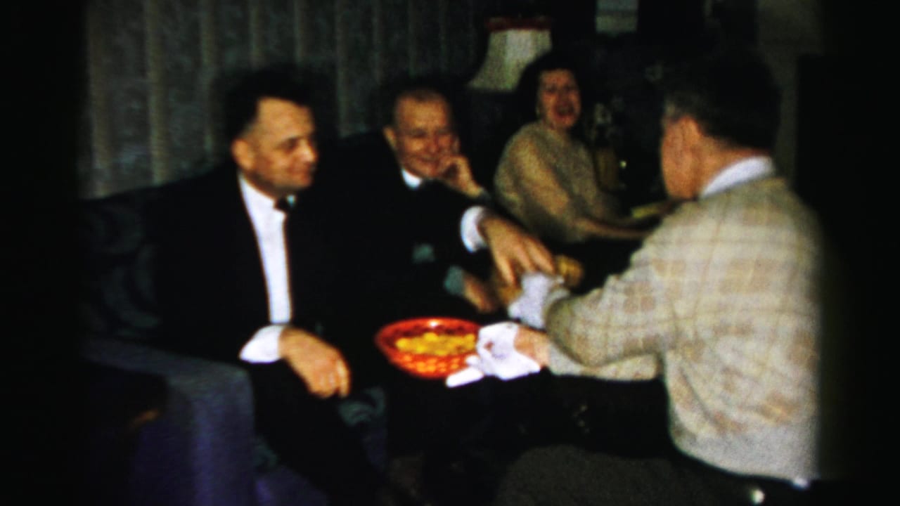 Guests sit together as a gloved man holds a red snack bowl near the group.