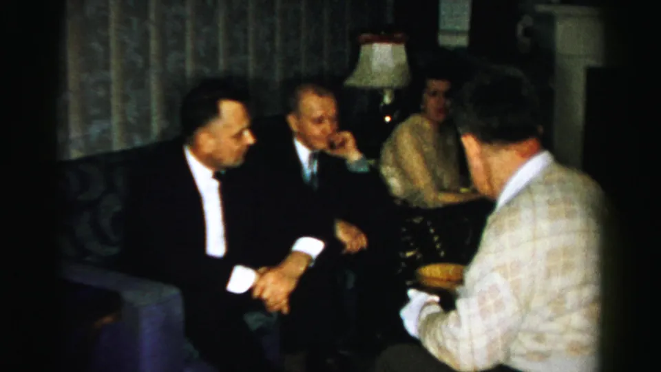A 1950s Albany living-room gathering shows suited men in conversation while a man with his back to camera holds a serving bowl.