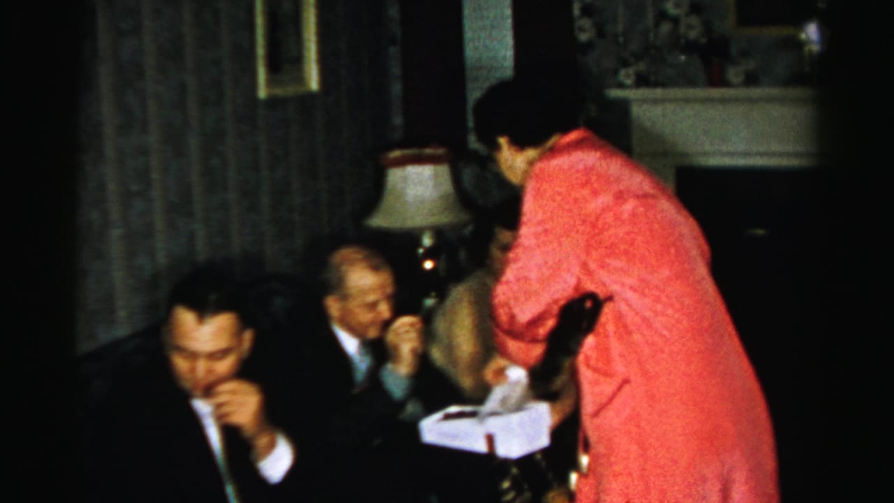 Woman in red leans toward seated guests while handling a white box.
