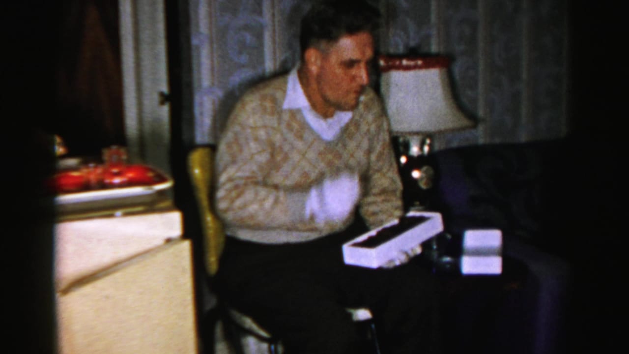 Man holds a white box with a dark chocolate piece visible inside.