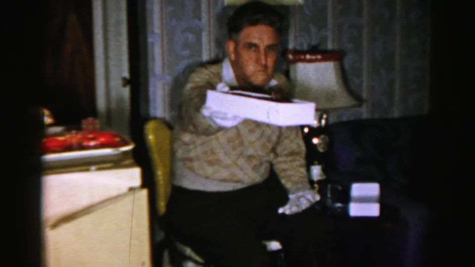 The man reaches forward with the white box as if offering the chocolate treat to the home-movie camera.