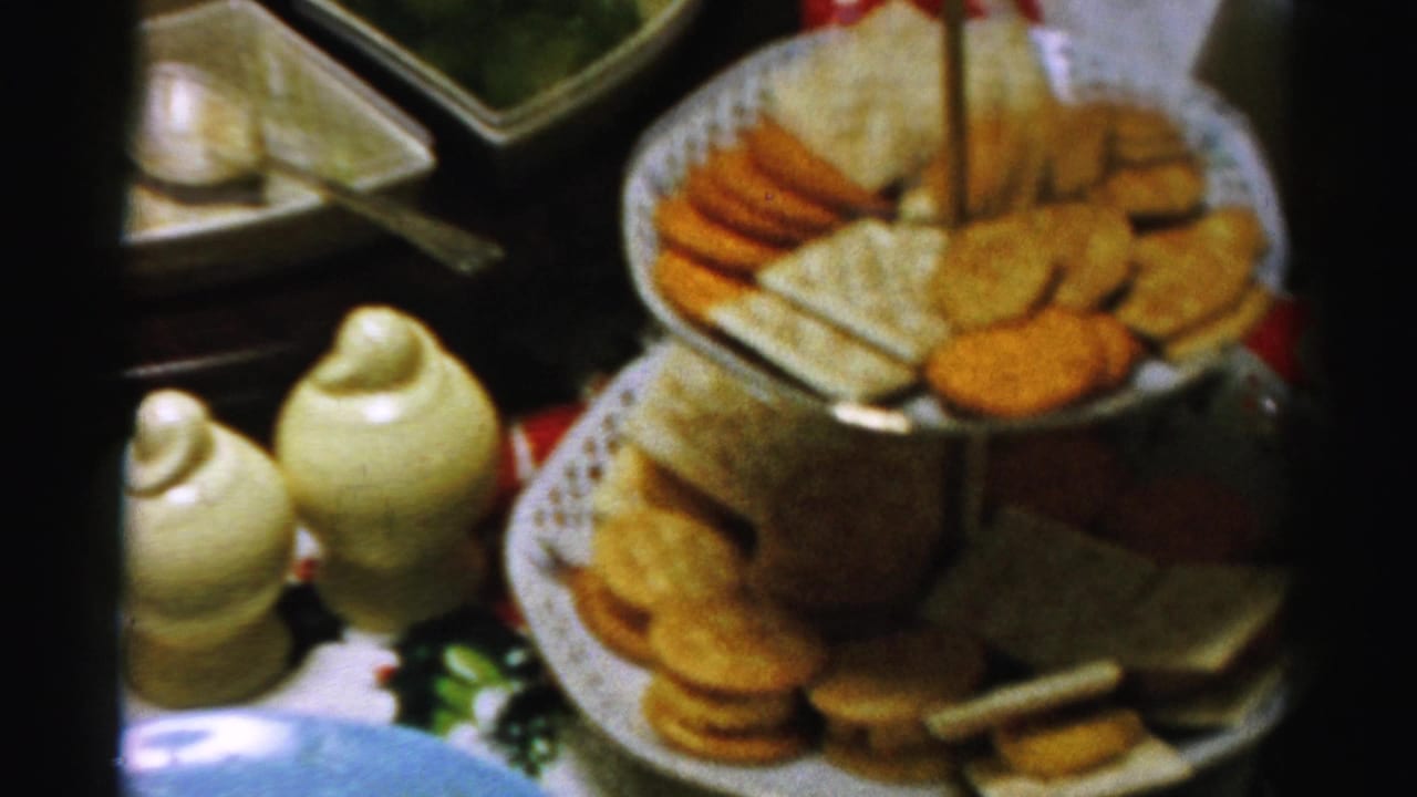 Tiered platter of crackers and cheese beside ceramic shakers and serving dishes on a party table.