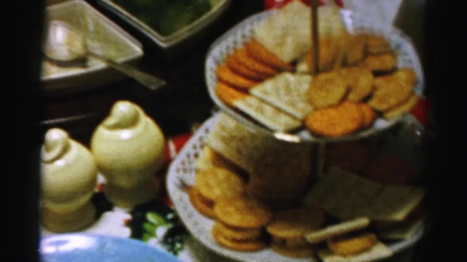 Close home-movie view of a 1950s Albany party table with crackers, cheese, ceramic shakers, and nearby serving dishes.
