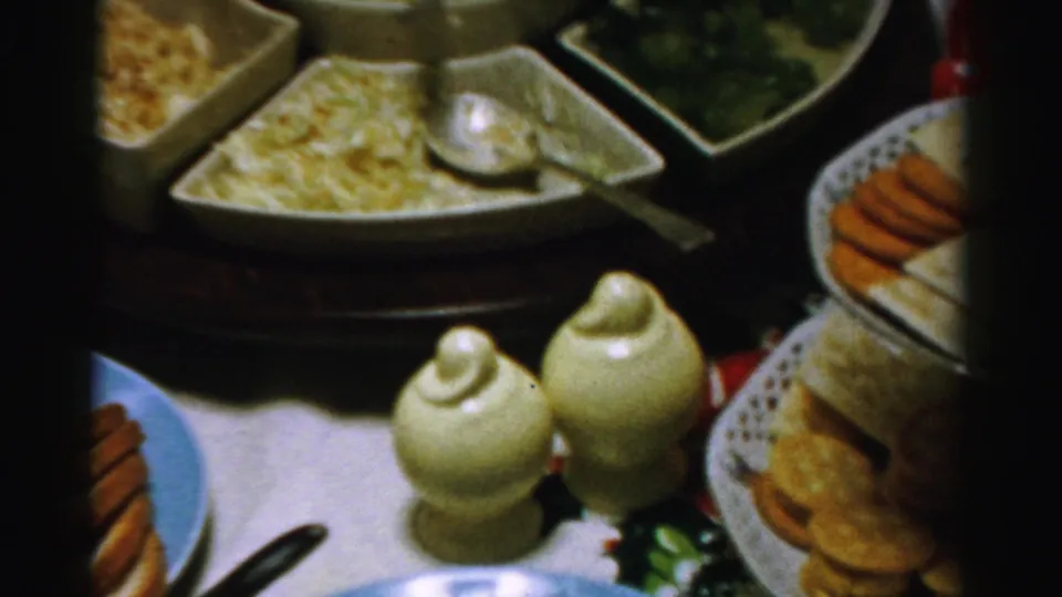 Albany-area 1950s home-movie frame showing a private party table with salad bowls, serving spoons, ceramic shakers, and crackers.