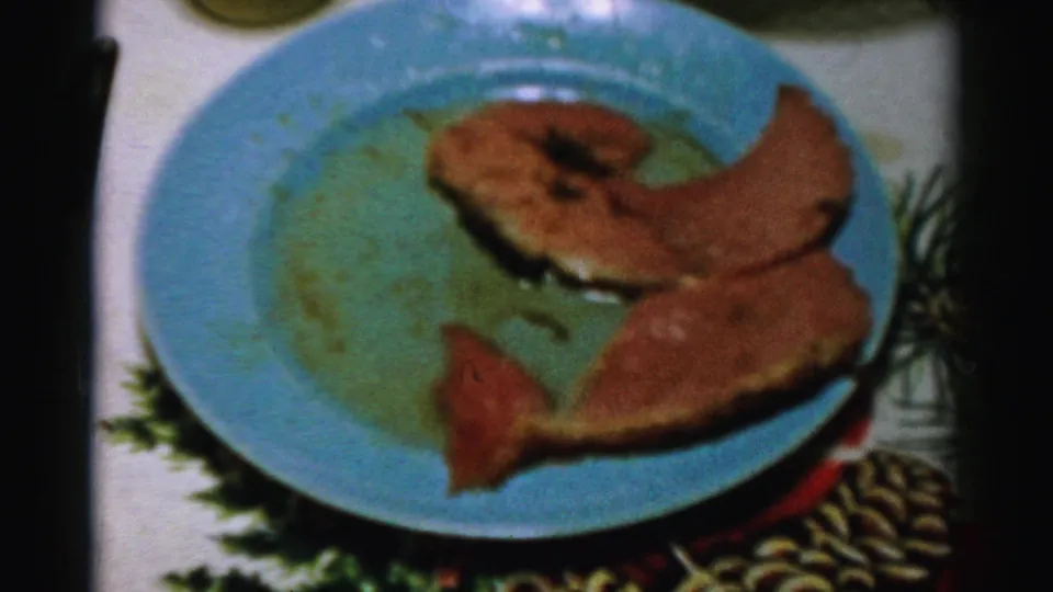 1956 Albany home-movie frame showing slices of meat on a blue plate set among holiday table linens and greenery.