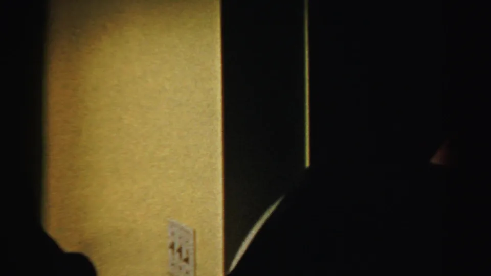 In Albany archival 8mm footage from the 1950s, two adult men appear in silhouette inside a dim room near visible wall switches.