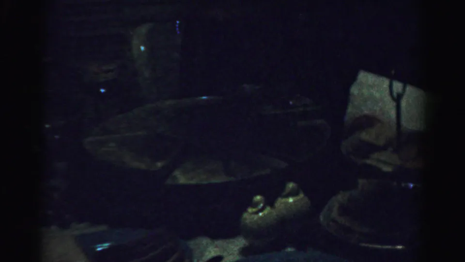 The camera turns toward a very dark interior area with a table or furniture surface and small household objects barely visible.