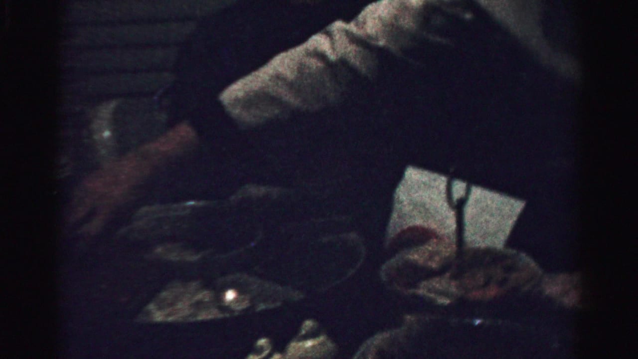A woman leans over a table with plates and candles in a dark room.