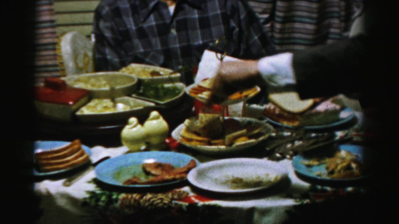 A hand reaches toward bread and condiments on a table filled with plates and serving dishes.
