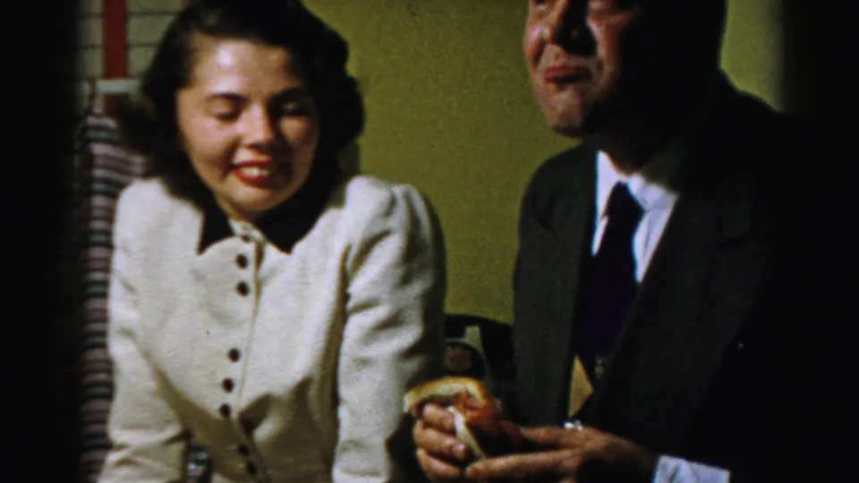 The Albany 1950s home-movie footage shows the woman smiling beside a suited man holding a sandwich after the comic eating moment.