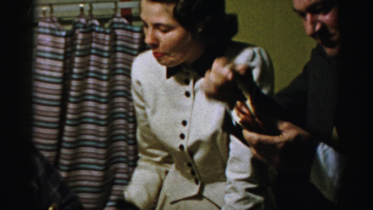 Woman watches a suited man lift a small food item near striped curtains.