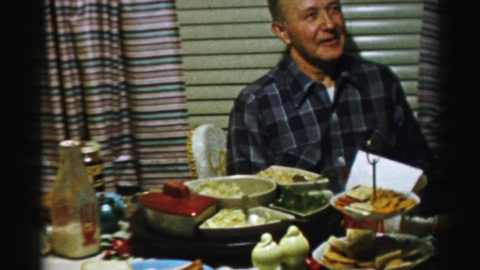 The same Albany dinner scene shows a smiling man in a plaid shirt seated near casseroles, a bottle, cups, and striped curtains.