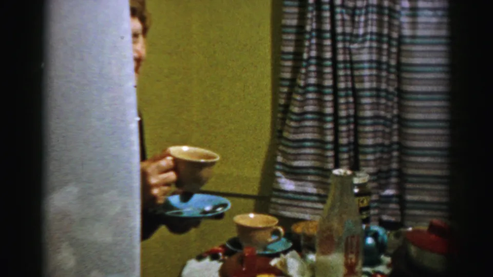 A partially obscured adult holds a cup beside the Albany dining table, with cups, a glass bottle, curtains, and dishes visible.