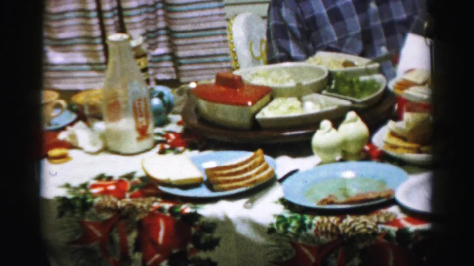 The home-movie frame shows a crowded Albany kitchen table with a bottle, serving dishes, plates, and festive table covering.