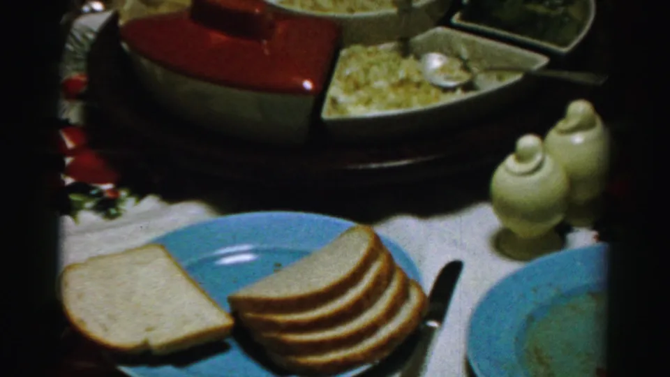 Final 1956 Albany frame of a holiday dining table with bread, blue plates, ceramic shakers, and covered dishes.