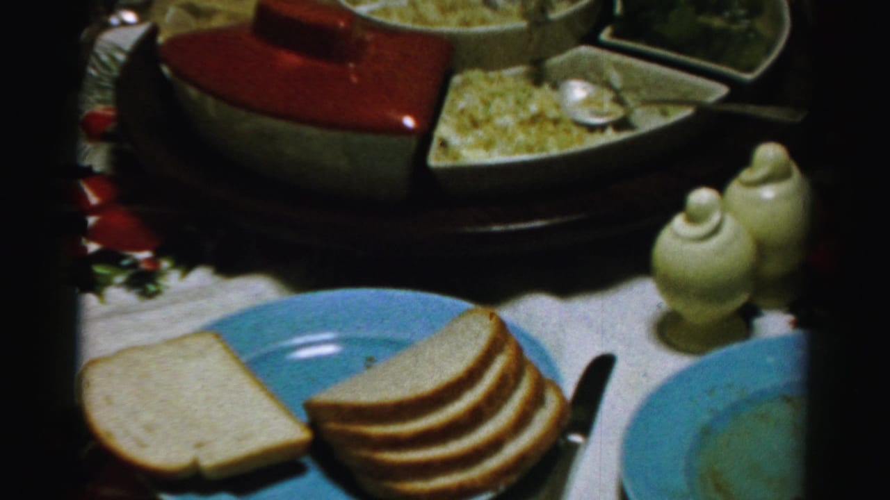Table setting with blue plates, sliced white bread, and a red-lidded serving dish.