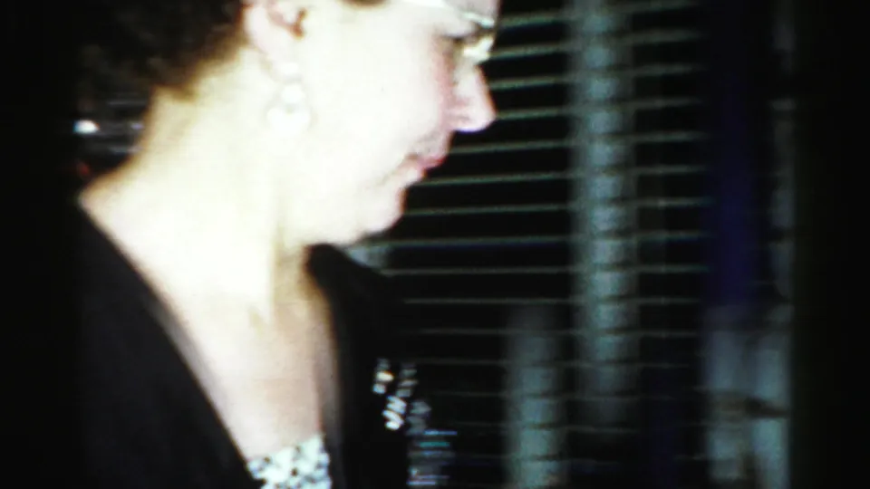 A close side view shows the woman with glasses and earrings beside window blinds in the Albany 1956 interior scene.