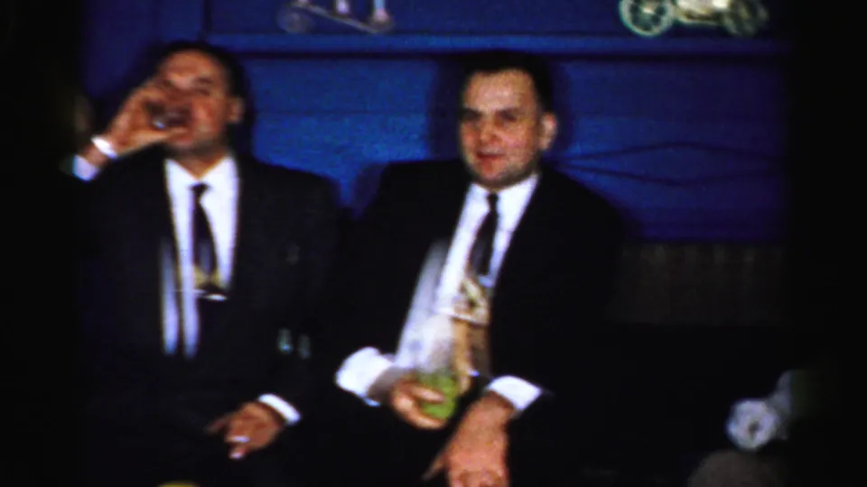 1950s Albany home-movie frame showing two suited men seated with drinks during a private holiday gathering.
