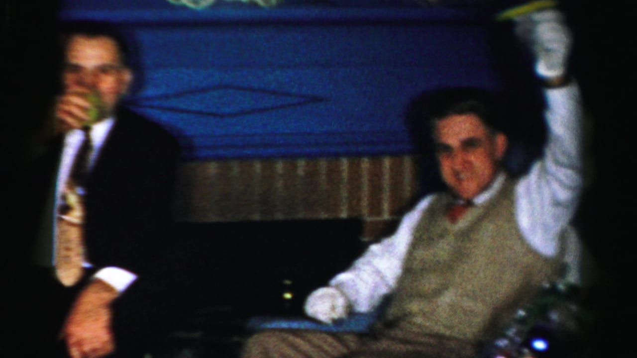 A suited man with a drink stands or sits near a gloved bell holder in a dim 1950s Albany party scene.