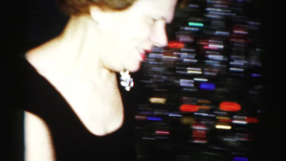 Close 1950s Albany home-movie frame of a woman in a black dress near a blurred surface with colorful small objects or refreshments.