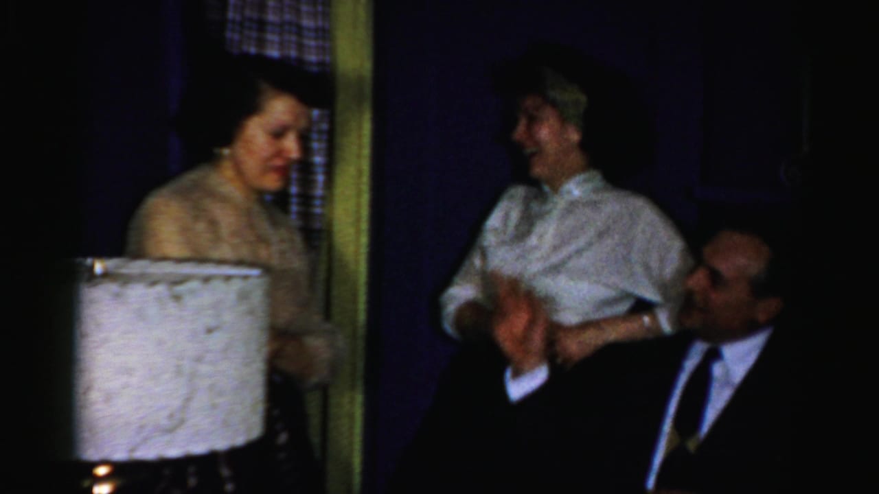 Three adults talking near a large white lampshade in a dim private room.