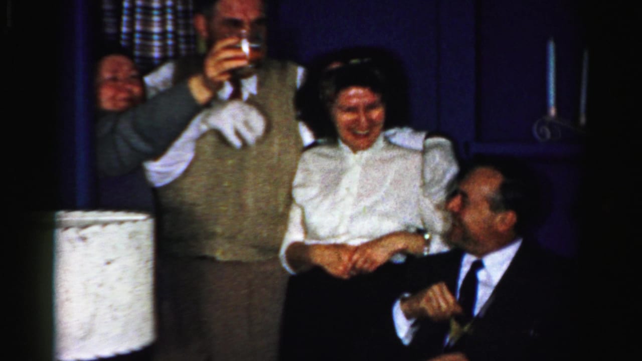 1950s Albany party footage shows a man lifting a drink, a woman laughing, and a seated man turning toward her in a dim private interior.