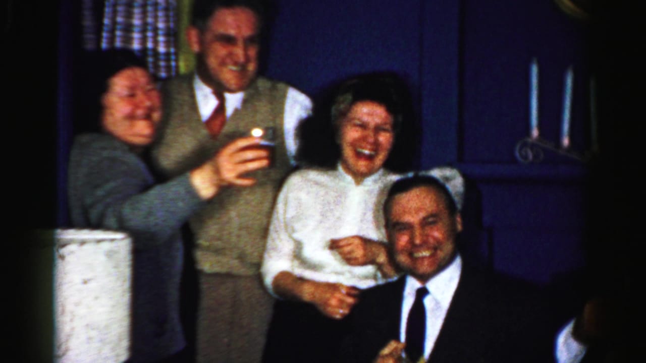 In this Albany, New York 1956 home-movie frame, four adults gather indoors as two raise drinks and the group laughs toward the camera.