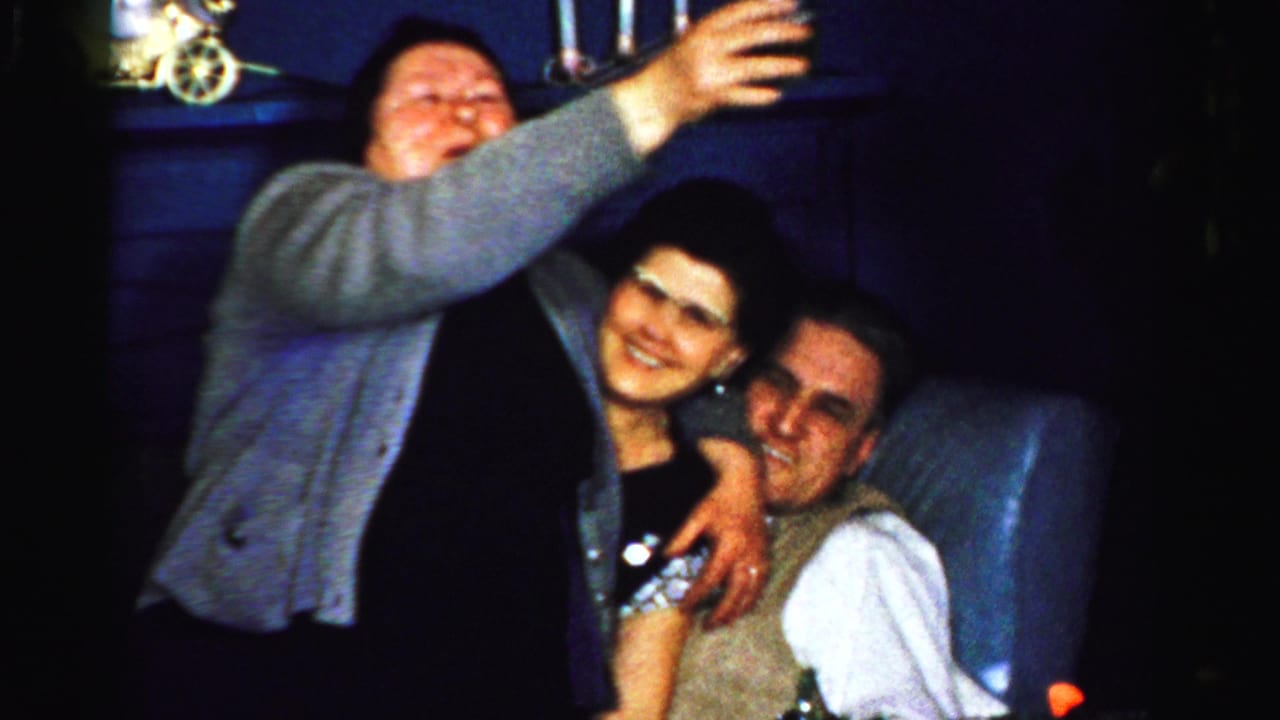 A woman reaches forward with a glass while two adults smile beside her.