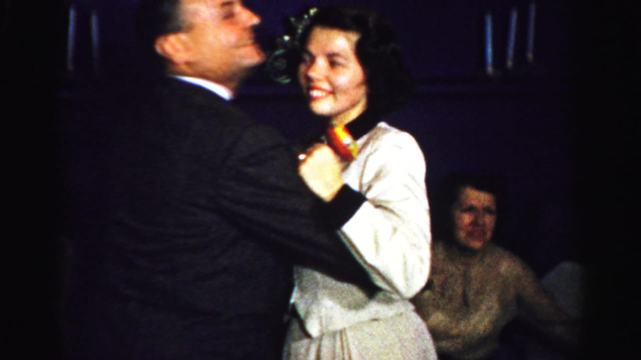 Smiling woman in a white dress dances closely with a man in a dark suit.