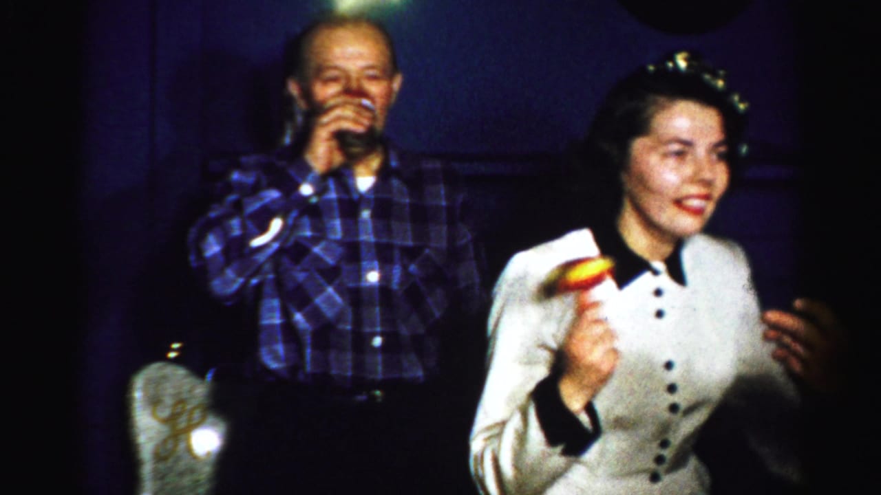Adults at an indoor party, including a man drinking and a woman holding a small noisemaker.