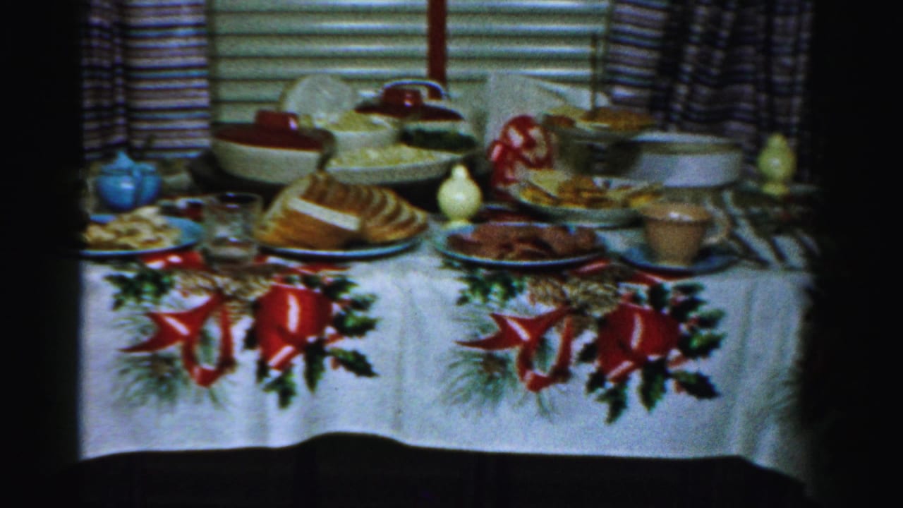 1956 Albany home interior with a food-laden holiday table, blue teapot, bread, bowls, glasses, and red bow tablecloth visible.