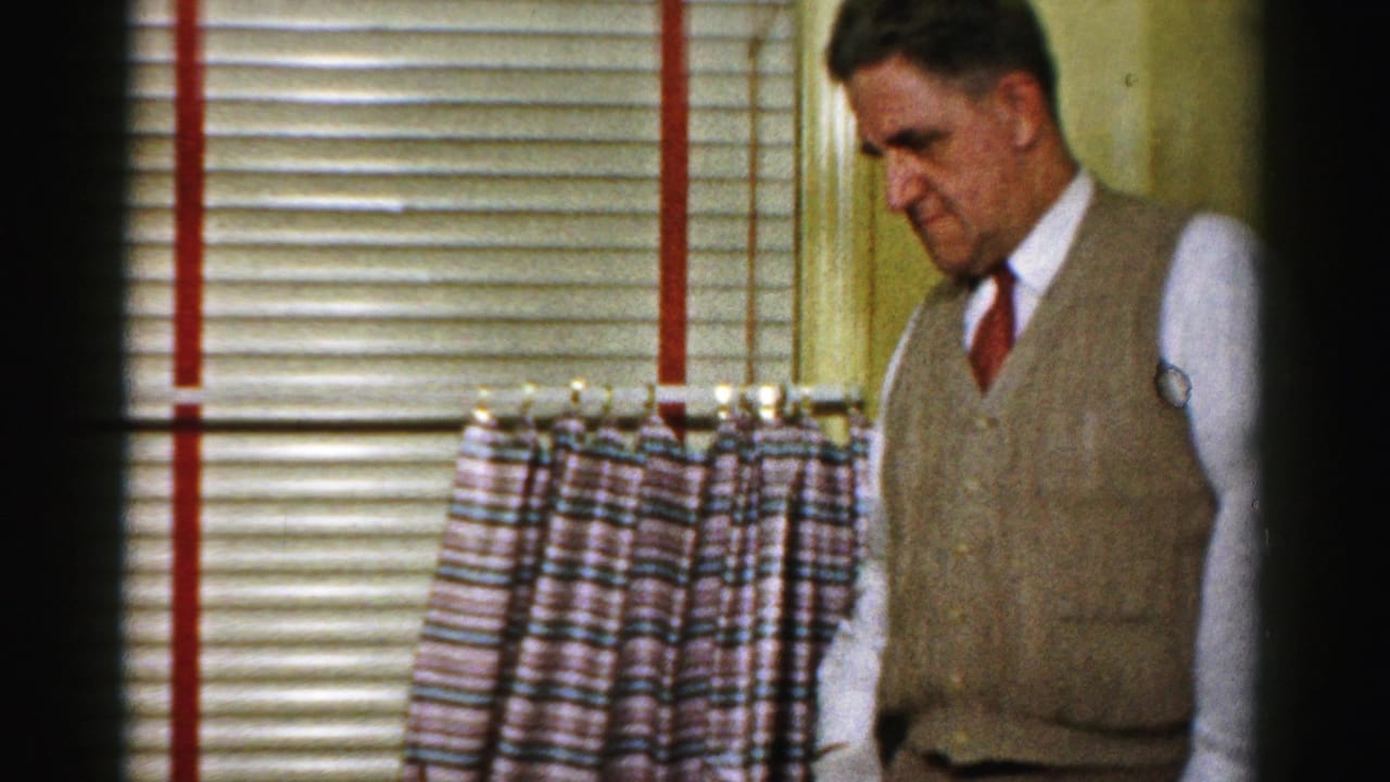 A man in a vest and tie stands beside venetian blinds and patterned curtains in the Albany kitchen scene.