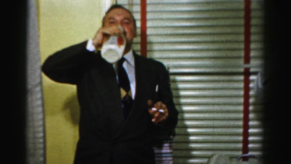 In the final frame, the suited man drinks from the milk bottle while holding a cigarette in the 1956 Albany kitchen.