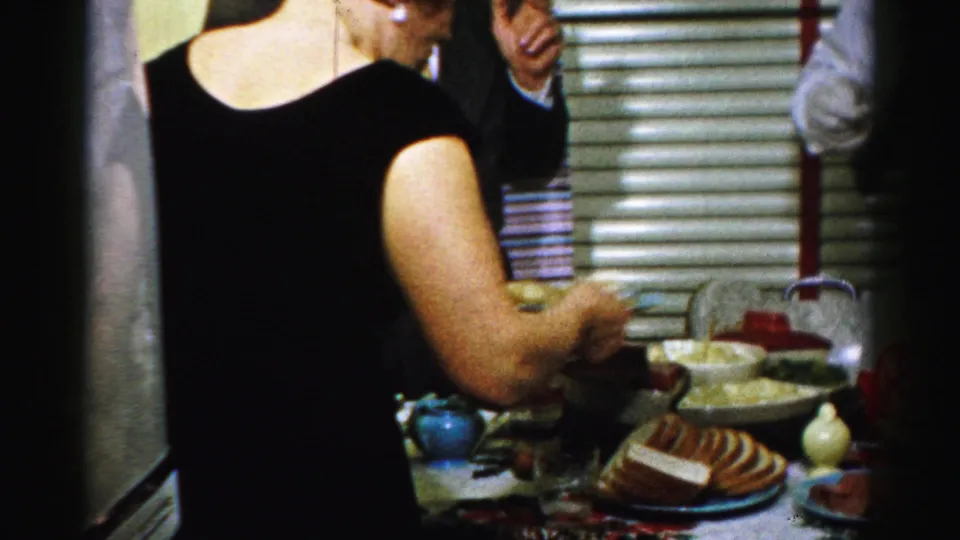 A woman in a black dress serves food beside plates, bowls, and a loaf or cake in a private Albany interior.