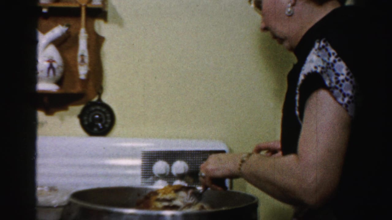 Woman prepares food at a large pot near a wall-mounted utensil rack and white stove.