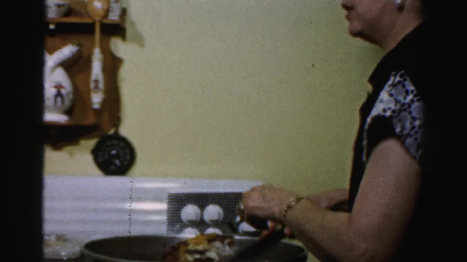 Side view of food preparation in a 1950s Albany private kitchen with hanging utensils and a large pot.